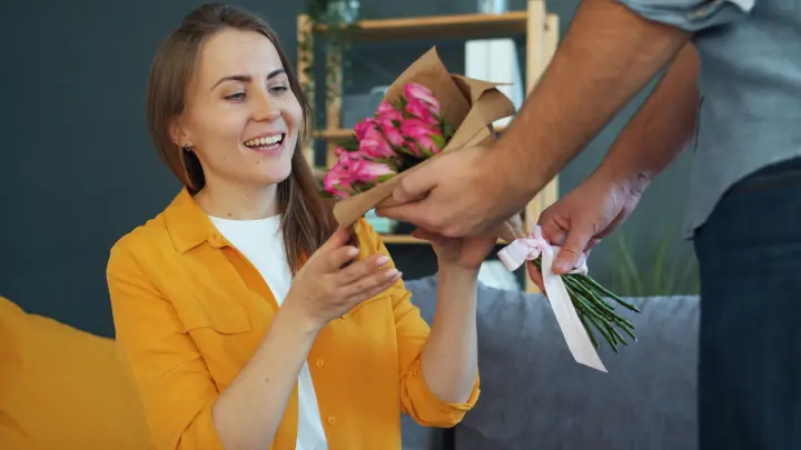 Mujer sonriente recibiendo un ramo de flores rosadas