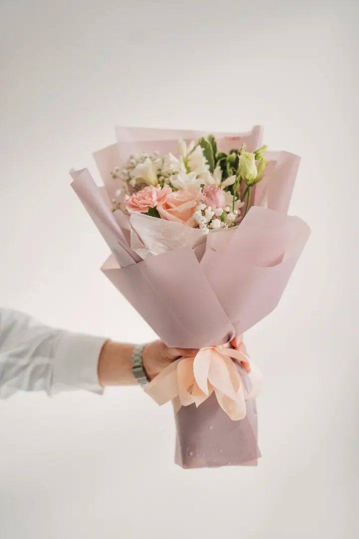 Mano sosteniendo un bouquet rosado envuelto en papel